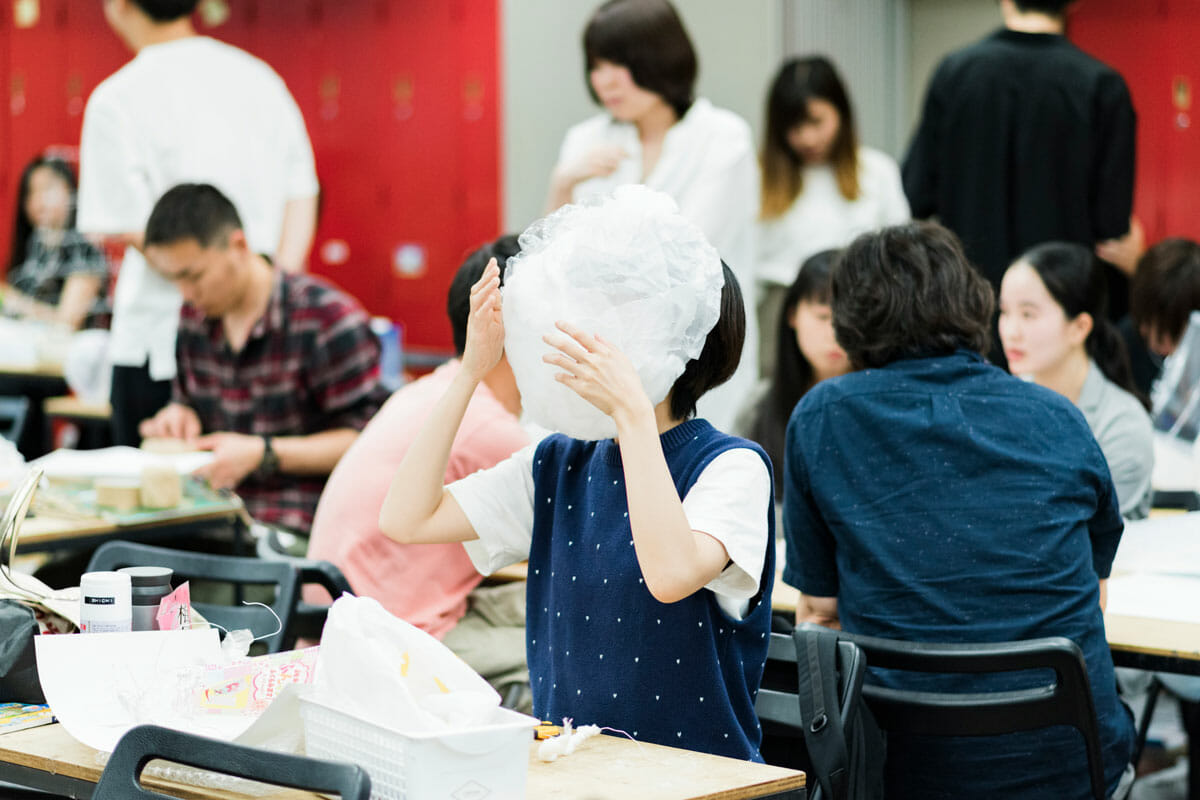 田辺さんが受け持つ1年生の造形課題「ルーツの翻訳」授業風景。 身の回りにあるものを使って頭部、あるいは身体の一部を覆う空間を作成し、自分の精神的なルーツを具体的な空間に翻訳することで、他者にも体験してもらう授業。