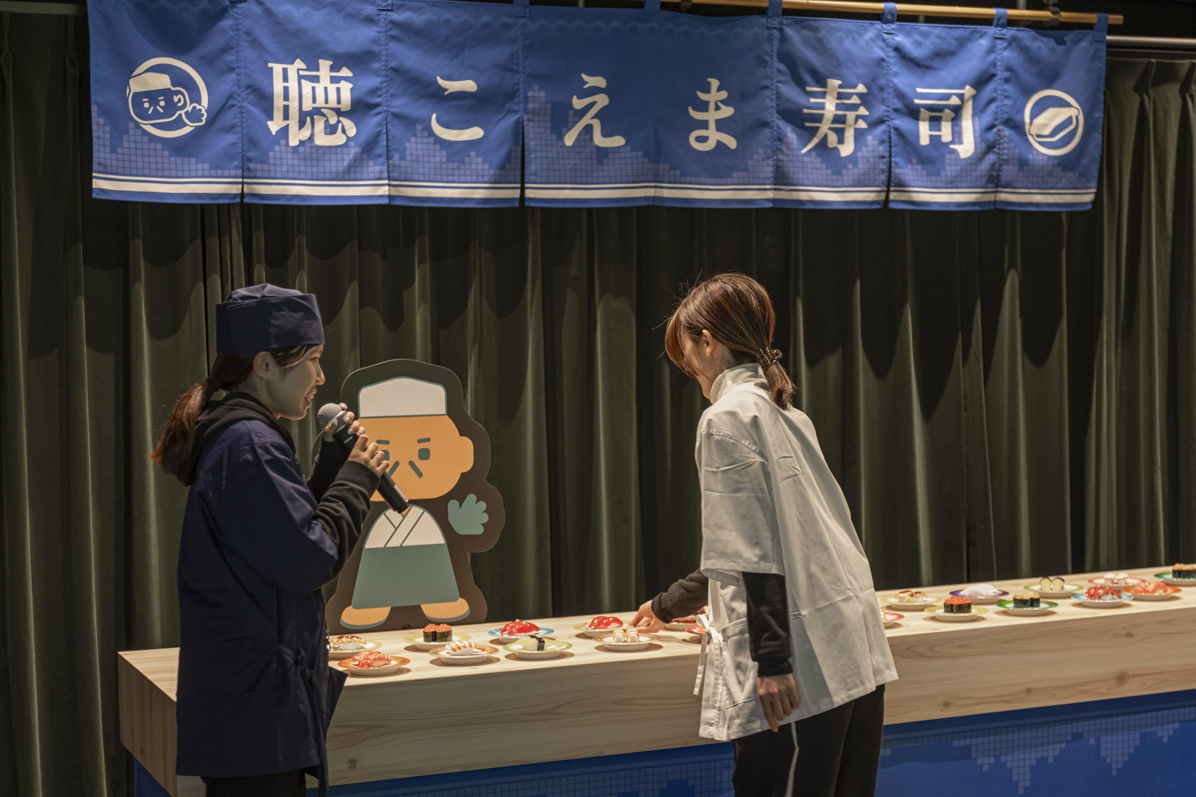 のれんや板前のキャラクターが設置されていたり、スタッフが寿司屋の店員の衣装を身に着けている様子